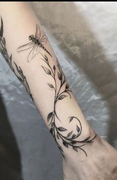 a woman's arm with a dragonfly and flowers tattoo on the left forearm