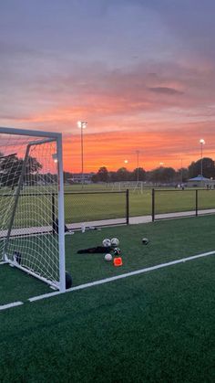 a soccer goal sitting on top of a field next to an orange and pink sky