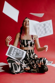 a woman is sitting on the floor with papers flying around her and reading a book