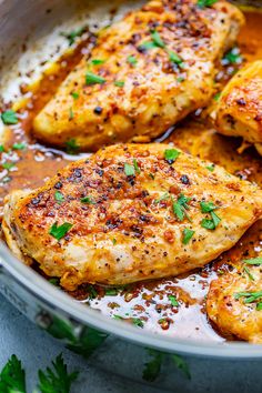 some chicken is cooking in a pan with sauce and parsley on the side,