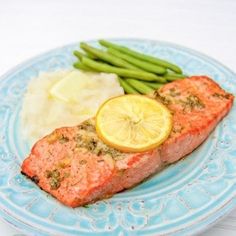 a blue plate topped with salmon, mashed potatoes and green beans next to a slice of lemon