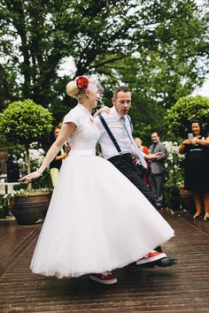 a man and woman in wedding attire dancing on a wooden deck with confetti