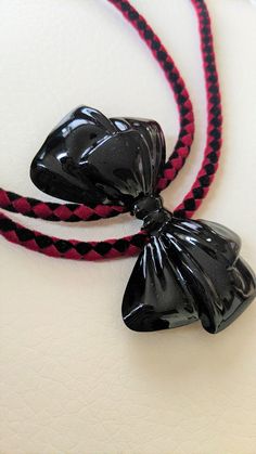 A black shiny bow over red and black velour cord makes this piece pop! Finished off with black enamel tips, you can wear this with any of your punk, rockabilly, goth, combos! 18.5"L, 2"H x 2.75"W, 19g RockaBolos are made with love and incorporate vintage and/or handmade materials.  Please anticipate that each piece will have a story. They have character, a past, and maybe even "imperfections".  But this is wearable art. Who would want it any other way? Adjustable Black Bow Tie For Party, Adjustable Black Bow For Black Tie Events, Black Ribbon Bow For Gifts, Adjustable Black Bow With Ribbon, Black Bow Tie With Ribbon For Gift, Black Ribbon Bow Tie For Evening, Black Ribbon Bow Tie For Gift, Black Ribbon Bow For Evening, Rockabilly Goth