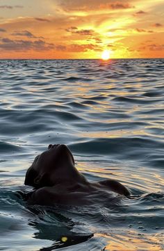 a person floating in the ocean at sunset with their head above the water's surface