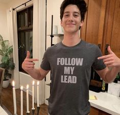 a young man standing in front of a cake with candles on it and giving the thumbs up