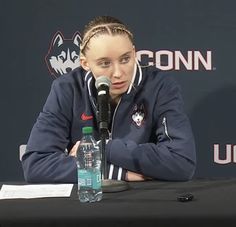 a woman sitting at a table in front of a microphone and holding a water bottle