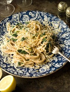 pasta with parmesan cheese and herbs on a blue plate next to lemon wedges