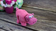 a pink stuffed animal sitting on top of a wooden table next to flowers and potted plants