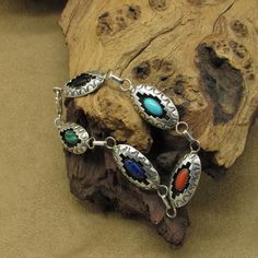 This vintage sterling silver bracelet is a stunning piece of jewelry that showcases intricate craftsmanship. The bracelet features a malachite, lapis lazuli, coral, turquoise, and onyx stones bezel set in a shadow box design. The bracelet measures 8 1/8" end to end. The stones measure 10.5mm wide and 5.5mm tall. The shadow boxes measure 1 3/8" wide including the bails and just over 1/2" tall. The artist's hallmark (J) is stamped on the back of the malachite shadow box. (STERLING) is also stamped Southwestern Silver Bracelets With Natural Stones, Collectible Silver Bracelets With Natural Stones, Southwestern Multi-stone Bracelet Jewelry, Southwestern Silver Multi-stone Bracelets, Southwestern Silver Bracelet With Multi-stone, Southwestern Silver Multi-stone Bracelet, Multicolor Inlay Sterling Silver Bracelets, Multicolor Sterling Silver Bracelet With Inlay, Multicolor Sterling Silver Bracelets With Inlay