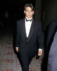 a young man in a tuxedo walking down a hallway with his hand in his pocket