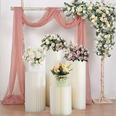 three white vases with flowers in them on a wooden floor next to pink drapes