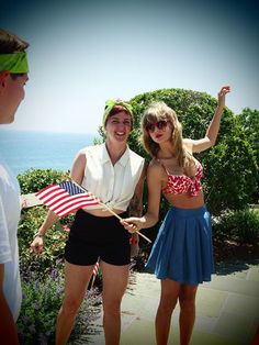 two people standing next to each other with an american flag in front of the ocean