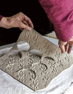 a woman is making an intricate design on a piece of clay that she's working on