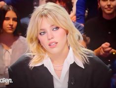 a woman with blonde hair and blue eyes sitting in front of a group of people