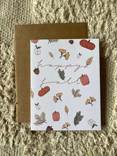 a white card with autumn leaves and acorns on it, next to a brown envelope