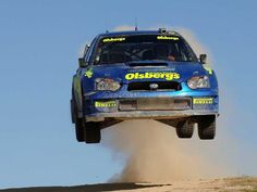 a blue car jumping in the air with dust coming out of it's tires