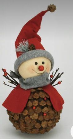 a snowman sitting on top of a pine cone covered in acorns and wearing a red hat