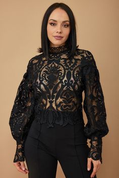 a woman wearing black pants and a sheer top with an intricate lace design on it