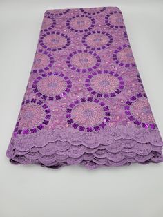 purple lace with flowers and sequins on the edges is laying on a white surface