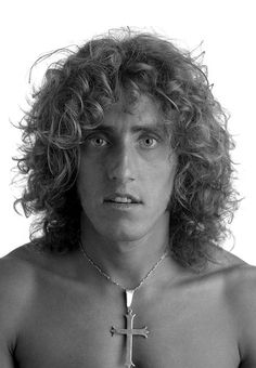 a shirtless man with long curly hair and a cross on his chest is looking at the camera