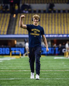 a man standing on top of a football field holding his hand up in the air