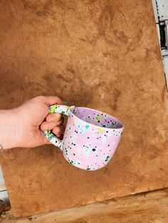 a hand holding a pink and white cup with sprinkles on the inside