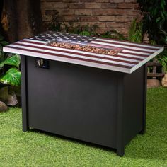 an american flag fire pit sitting on top of green grass next to a brick wall