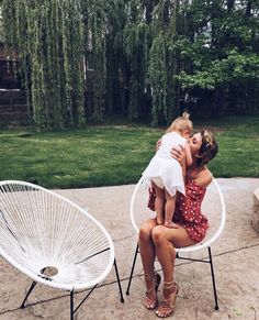 a woman sitting in a white chair holding a small child on her lap and kissing her cheek