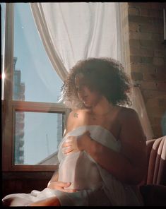 a woman sitting in front of a window with her arm wrapped around another woman's waist