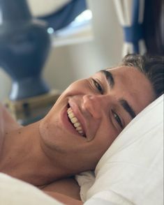 a man laying in bed with his eyes closed and mouth wide open, smiling at the camera