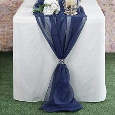 a table topped with a vase filled with flowers next to a blue cloth draped over it