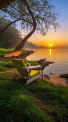 a lawn chair sitting on top of a lush green field next to the ocean at sunset