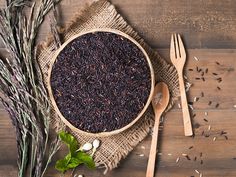 a wooden bowl filled with black rice next to two spoons