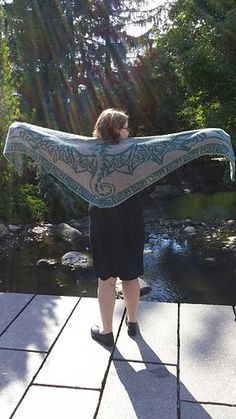 a woman is standing on a walkway with a scarf over her head and looking at the water