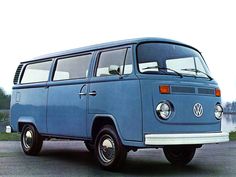 an old blue vw bus parked in a parking lot next to a body of water