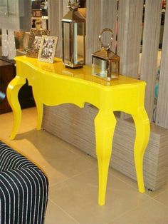 a yellow console table with pictures on it and a lamp next to it in a store