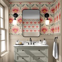 a bathroom vanity with two sinks and a large mirror above it, in front of a floral wallpaper