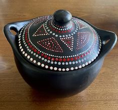 a black pot with red and white designs on it sitting on a wooden table top