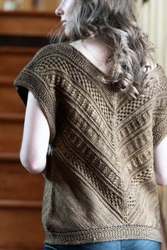 a woman standing in front of a dresser wearing a brown knitted sweater and jeans