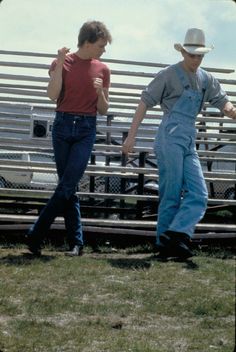 two men standing next to each other in front of a stadium bleachers with their arms outstretched