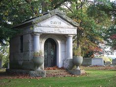 an old grave with two urns in front of it on the grass and trees