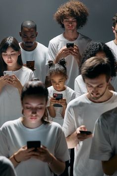 a group of people in white shirts looking at their cell phones while they stand together