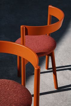 two orange chairs sitting next to each other on top of a cement floor in the sun