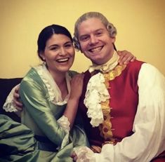 a man and woman dressed in period costumes pose for a photo together on a couch