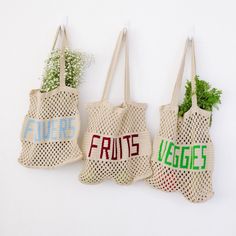 three bags with fruit and veggies written on them are hanging from the wall