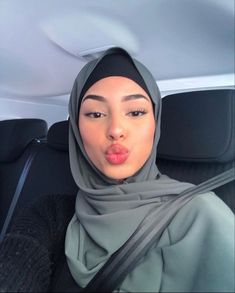 a woman sticking her tongue out while sitting in the back seat of a car wearing a hijab