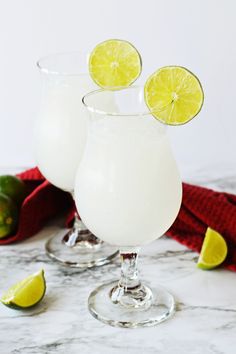 two glasses filled with white liquid and topped with limes on a marble counter top