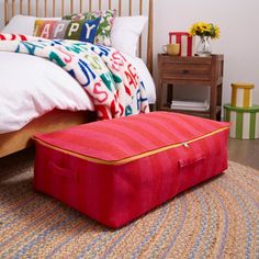 a bed with colorful pillows and blankets on top of it next to a red storage bag