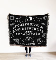 a person is holding up a black blanket with letters and numbers written in white on it