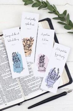 three bookmarks with plants on them sitting next to an open bible and some pens